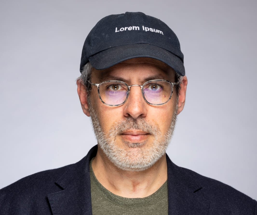 Portrait of Benoît Couty wearing glasses and a dark cap embroidered with Lorem ipsum.